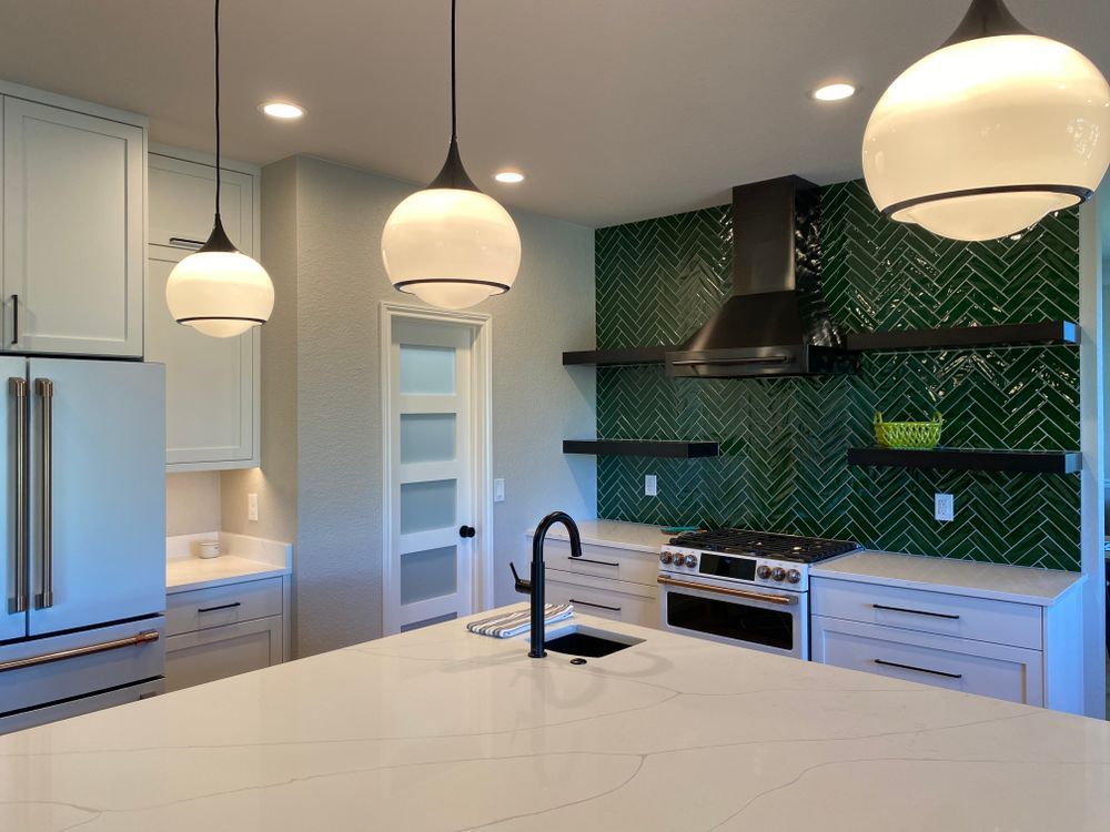 A kitchen with white cabinets and green tiles on the wall.
