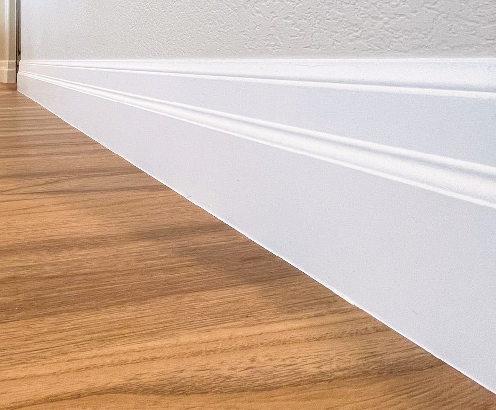 A close up of a white skirting board on a wooden floor.