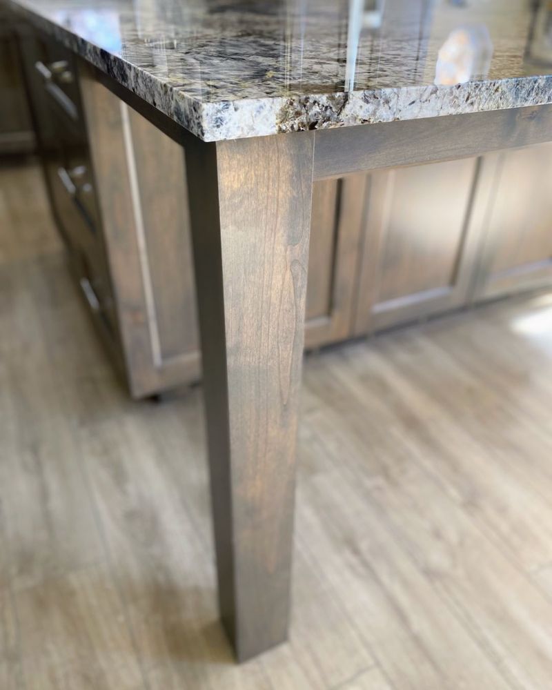 A kitchen island with a granite counter top and a wooden leg.