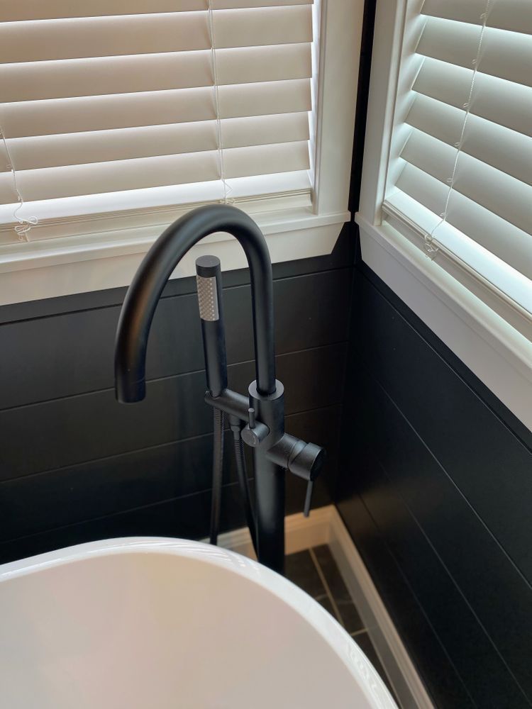 A black bathtub faucet in a bathroom next to a window.