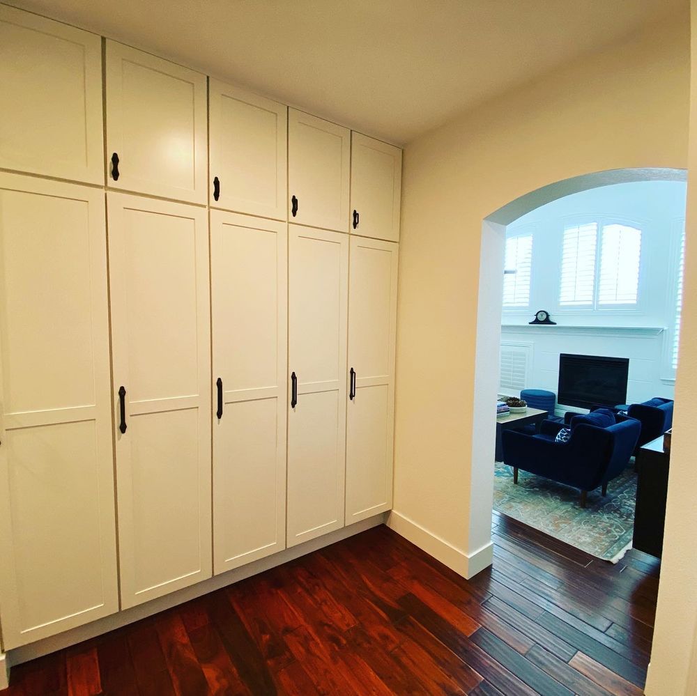 A hallway with white cabinets and hardwood floors leading to a living room.