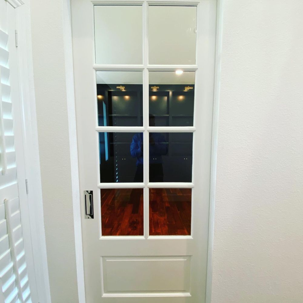A white door with a reflection of a person in it is in a hallway.