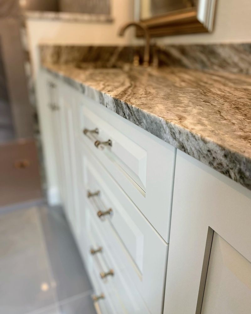A bathroom vanity with white cabinets and a granite counter top.