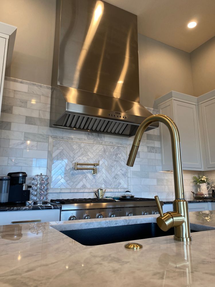 A kitchen with a stainless steel hood and a gold faucet