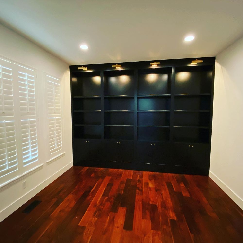 An empty room with hardwood floors and black shelves.