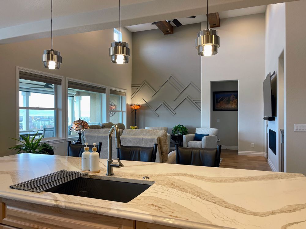 A kitchen with a sink , counter top , and a living room in the background.
