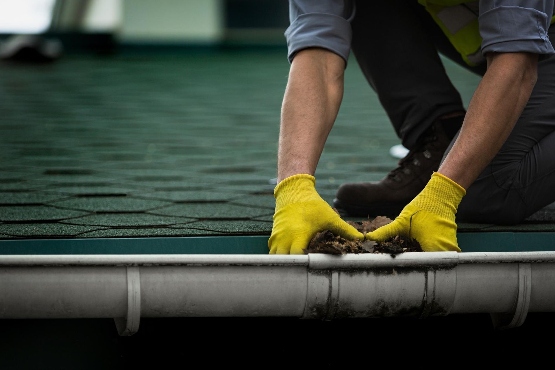 A man wearing yellow gloves is cleaning a gutter on a roof.