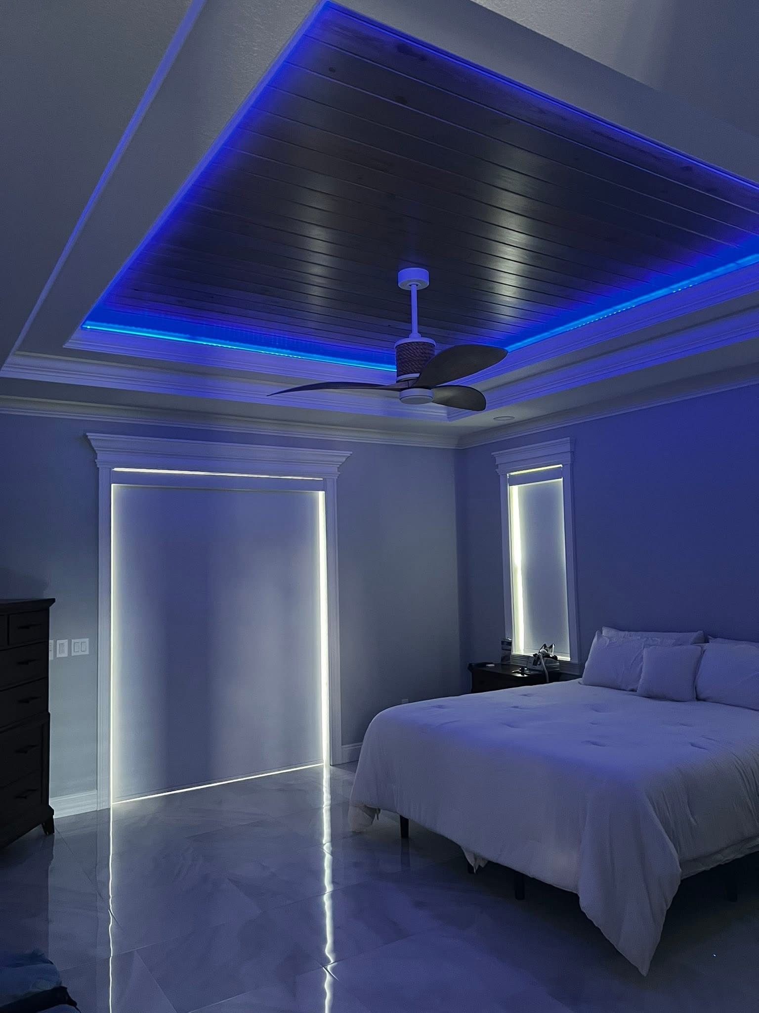 A modern bedroom with white bedding, polished floors, and a ceiling featuring a metallic patterned insert with blue lighting.