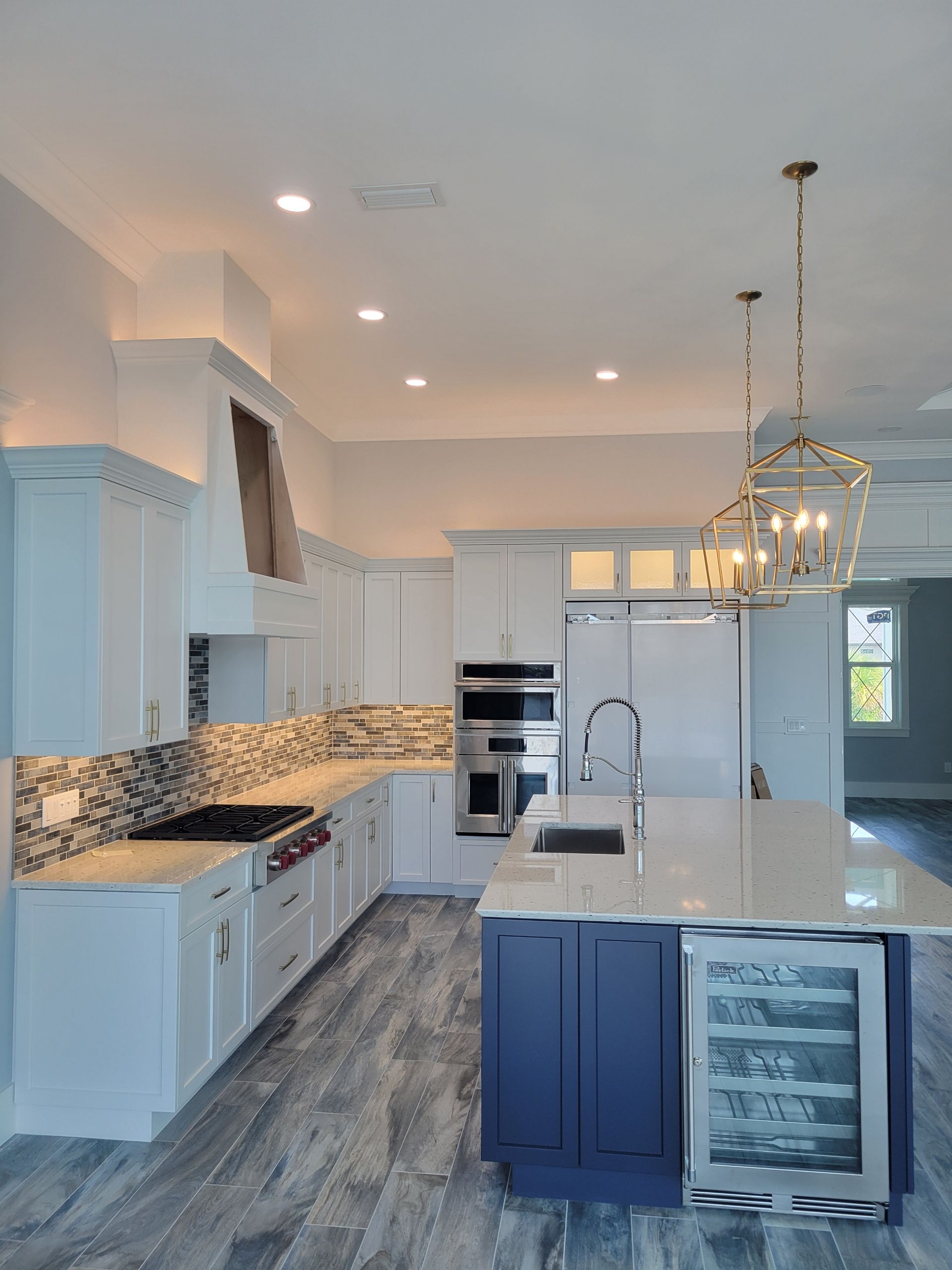 A white kitchen with a navy island, stainless steel appliances, marble countertops, and patterned backsplash.