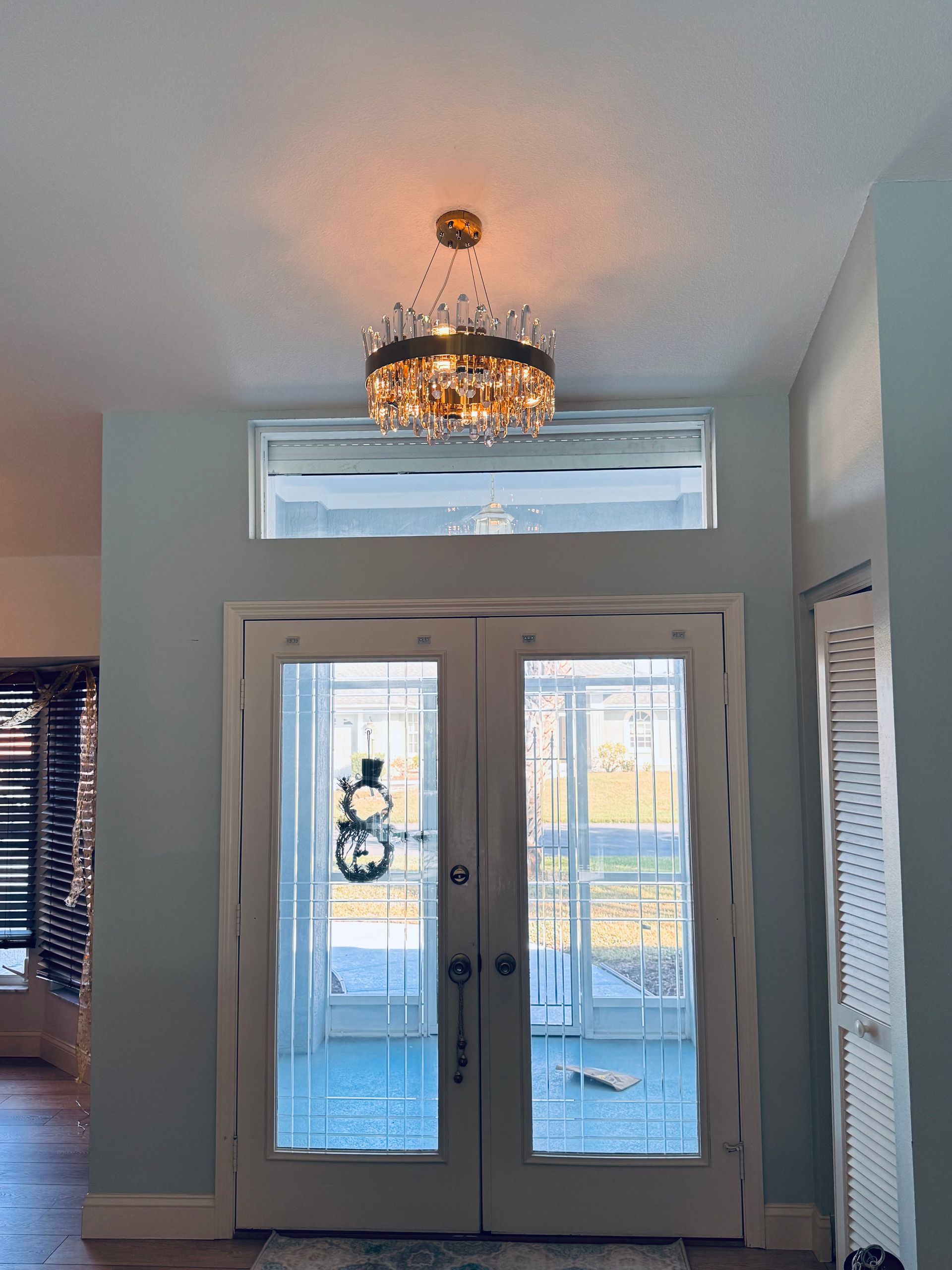 A light blue entryway with double glass doors, a large transom window, and a circular crystal chandelier above.