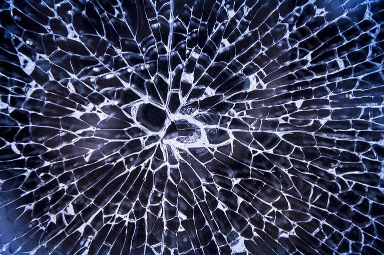 Broken glass, radiating cracks from the center, shards outlined in white against a dark blue background.
