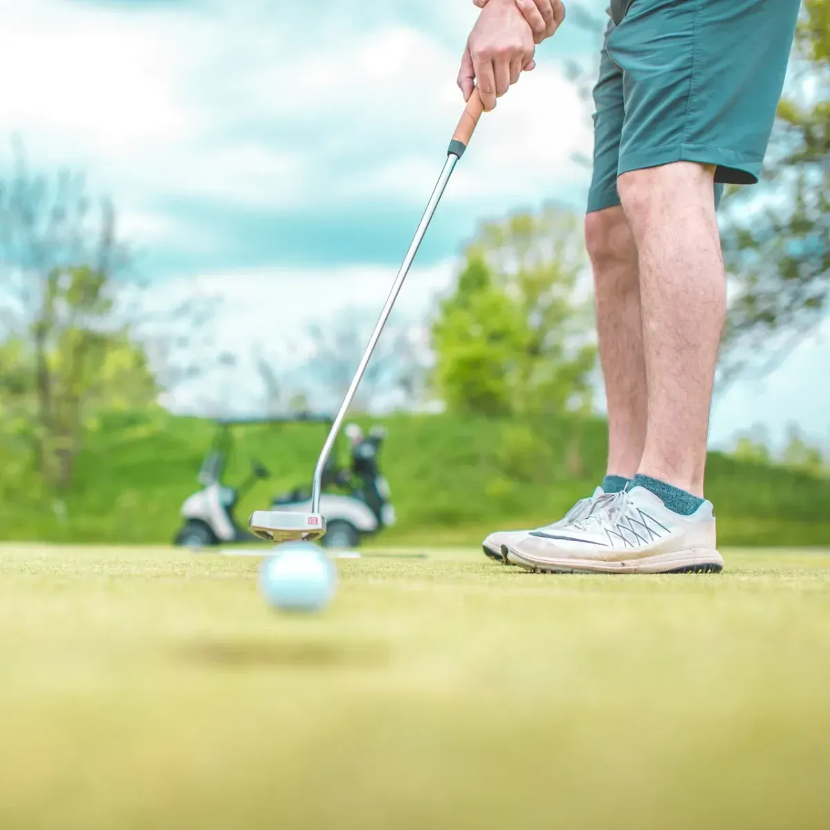 A man is putting a golf ball on a green with a golf cart in the background.