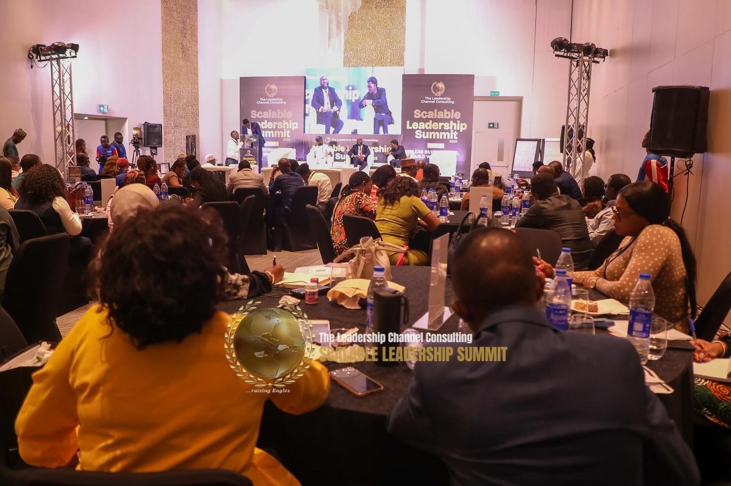 Conference with speakers on stage, attendees at tables, and 