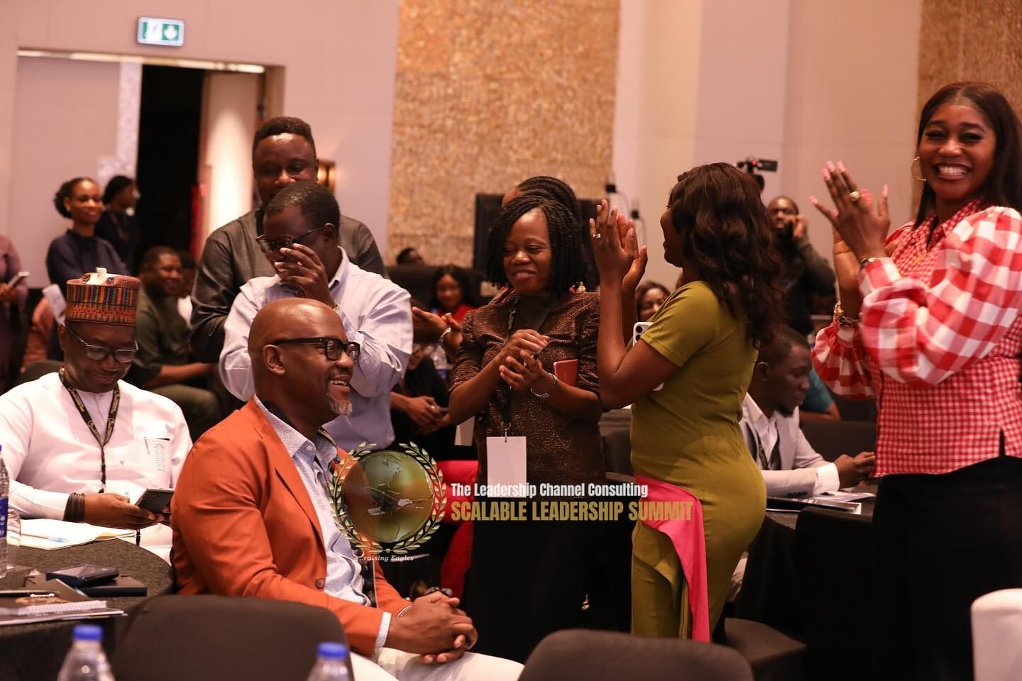 People celebrating an award ceremony. Man seated with trophy, others clapping. Festive setting.