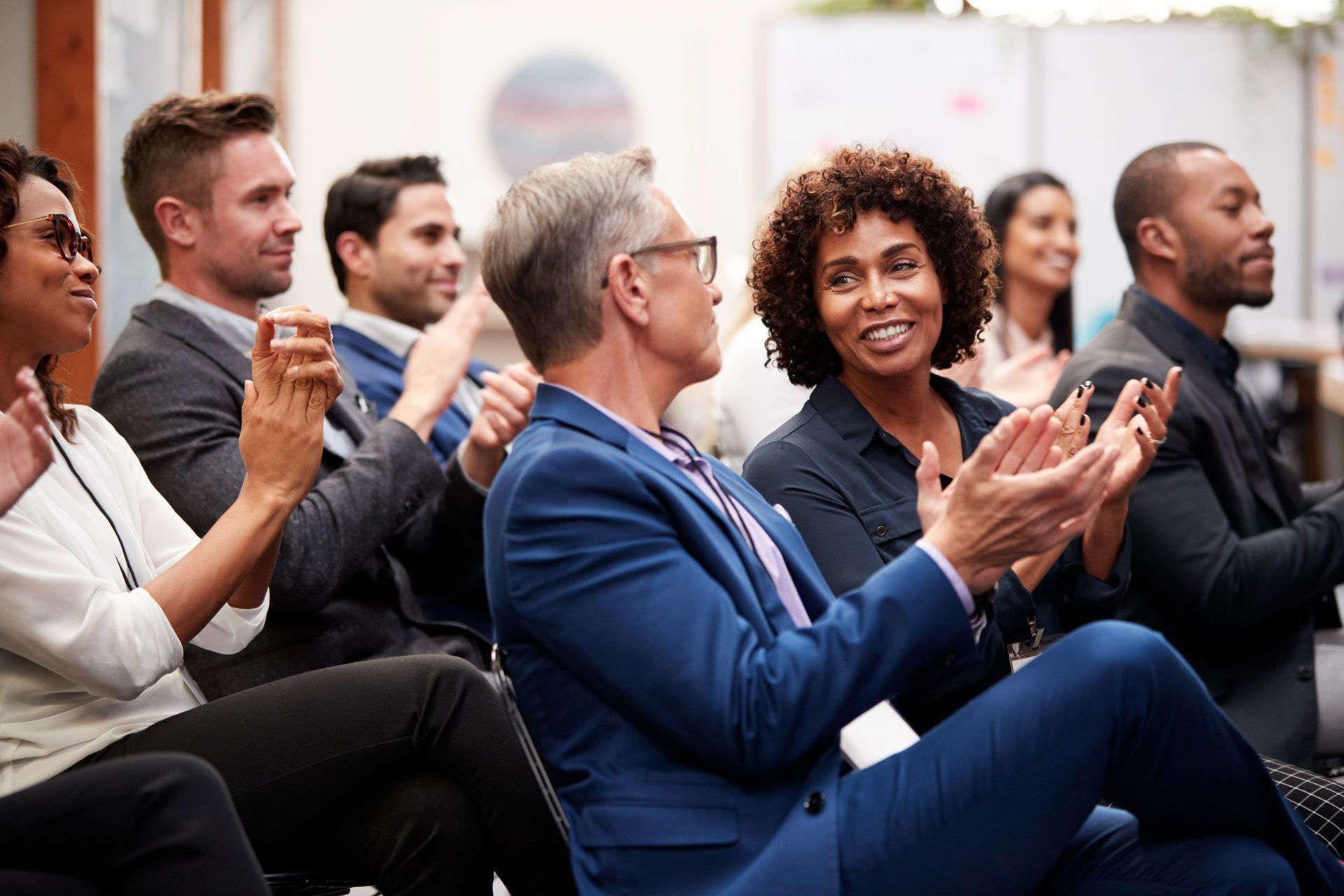 People clapping at a business conference, indoors. Smiling and engaged attendees in a well-lit setting.