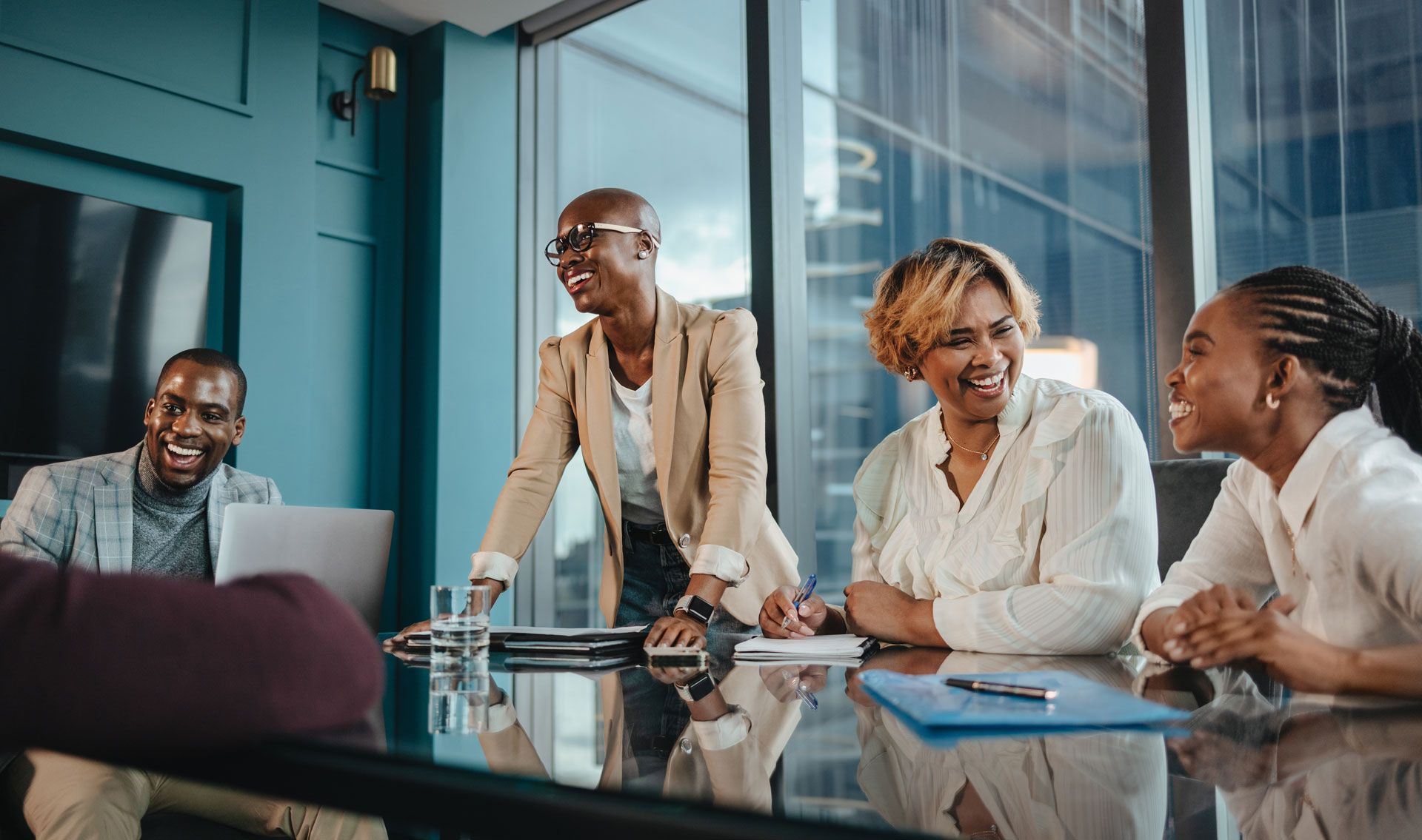 Diverse group of coworkers laughing around a conference table in an office.