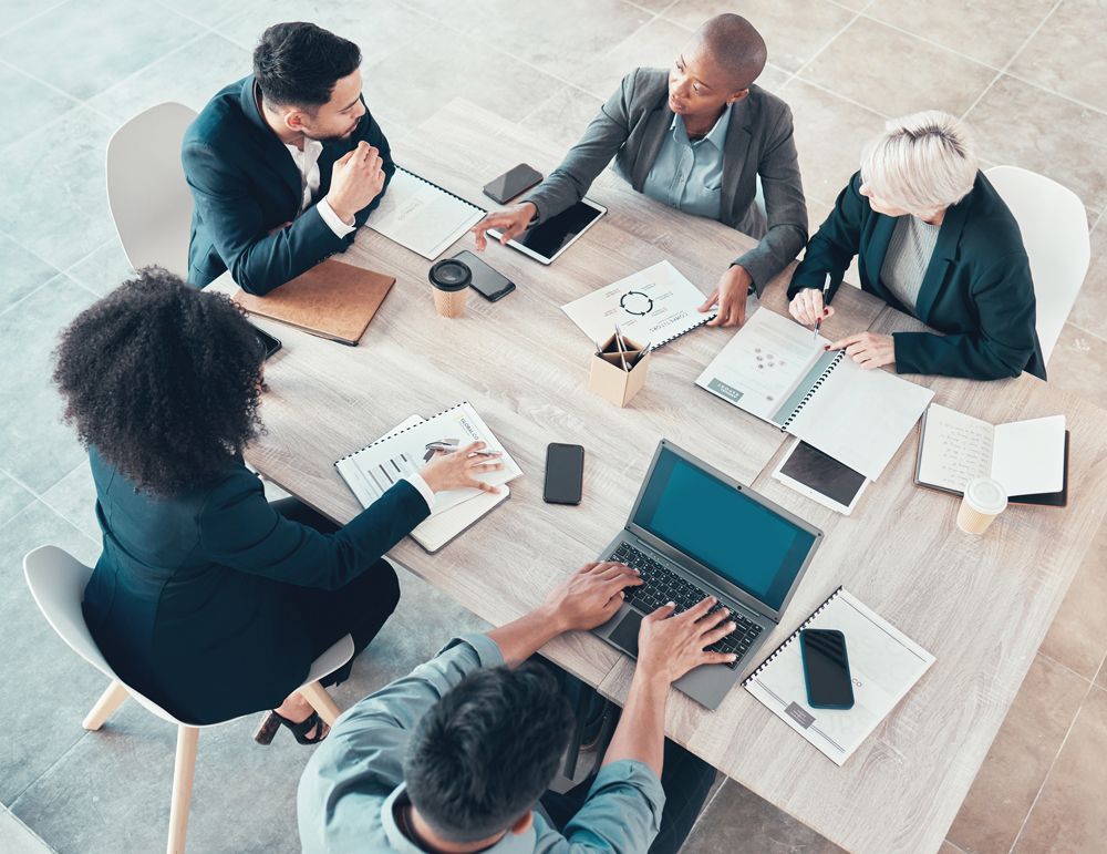 A group of people are sitting around a table with laptops.