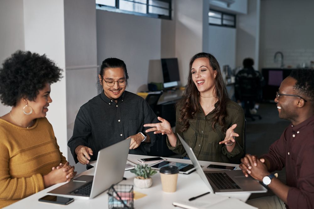 A group of people are sitting around a table with laptops.