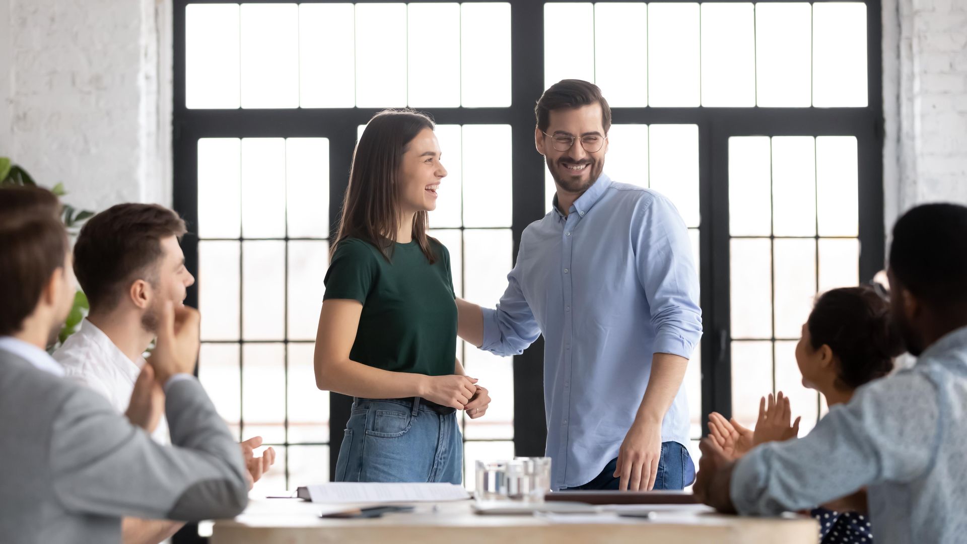 A man and a woman are shaking hands in front of a group of people.