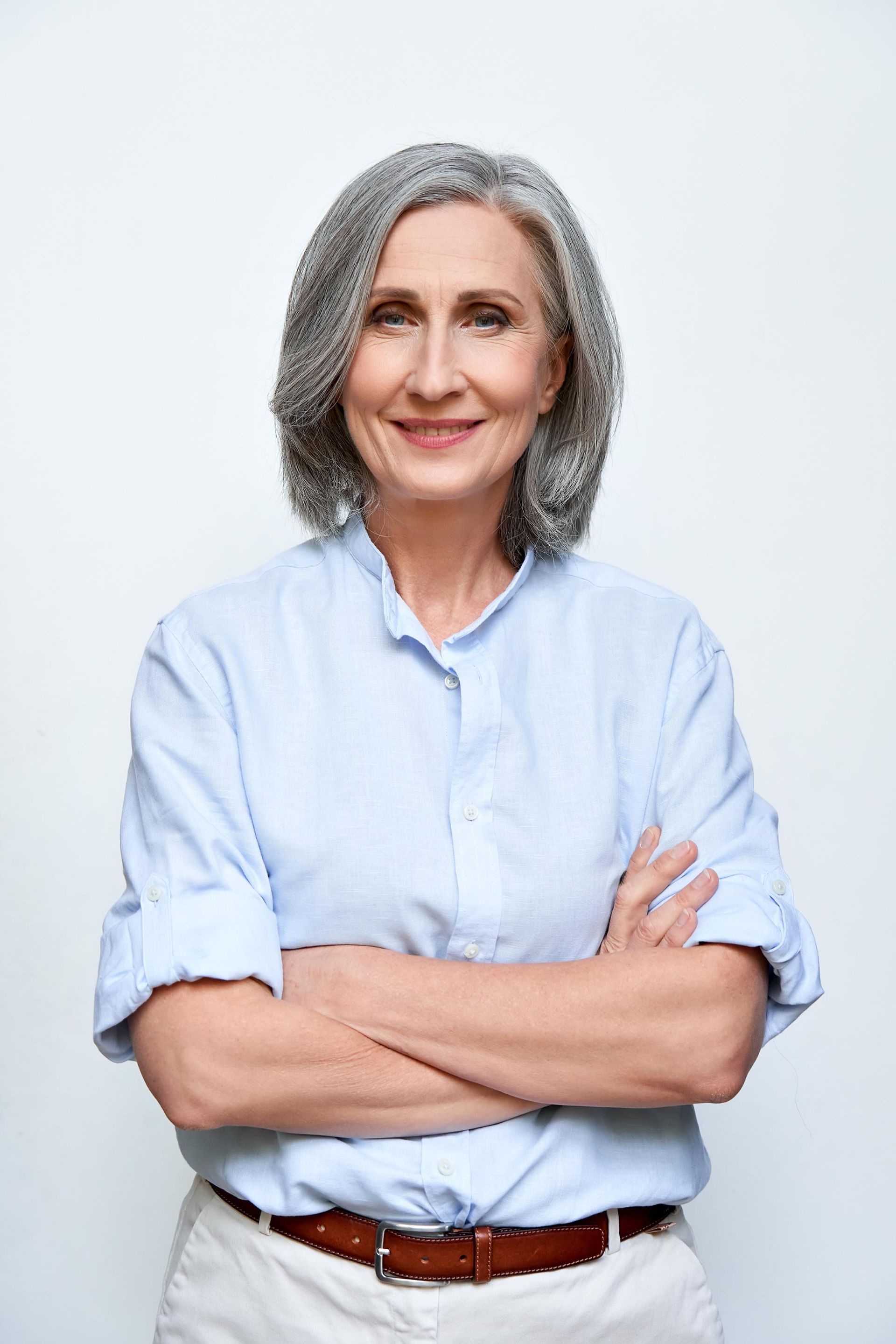 A woman with gray hair is standing with her arms crossed and smiling.