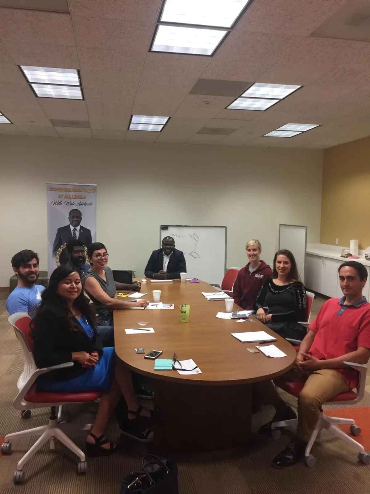 People seated around a conference table, attending a meeting. Various skin tones, casual attire, in an office setting.