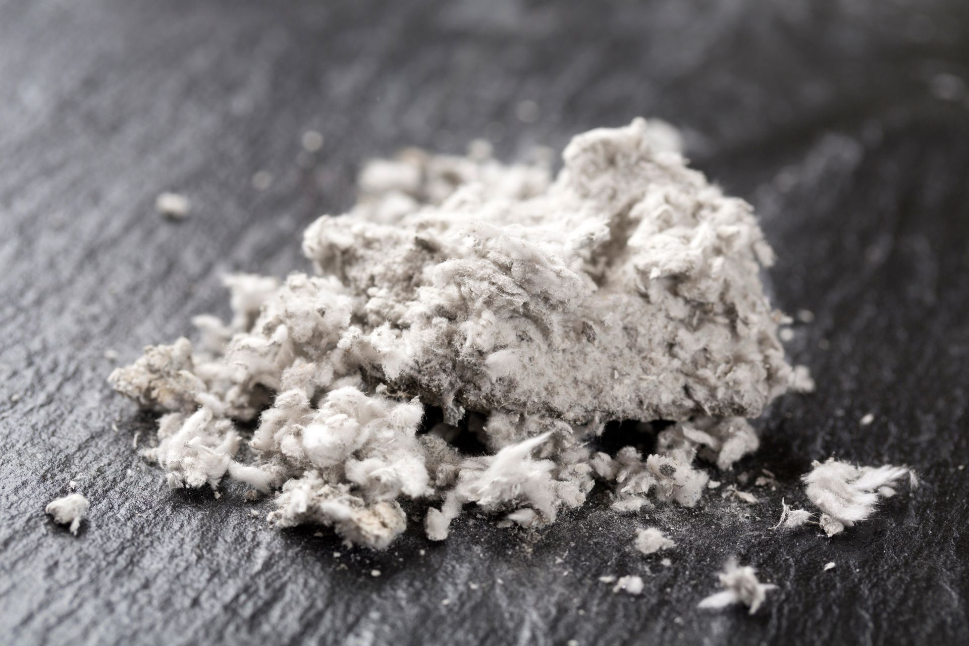 Pile of gray, fibrous material on a dark textured surface.