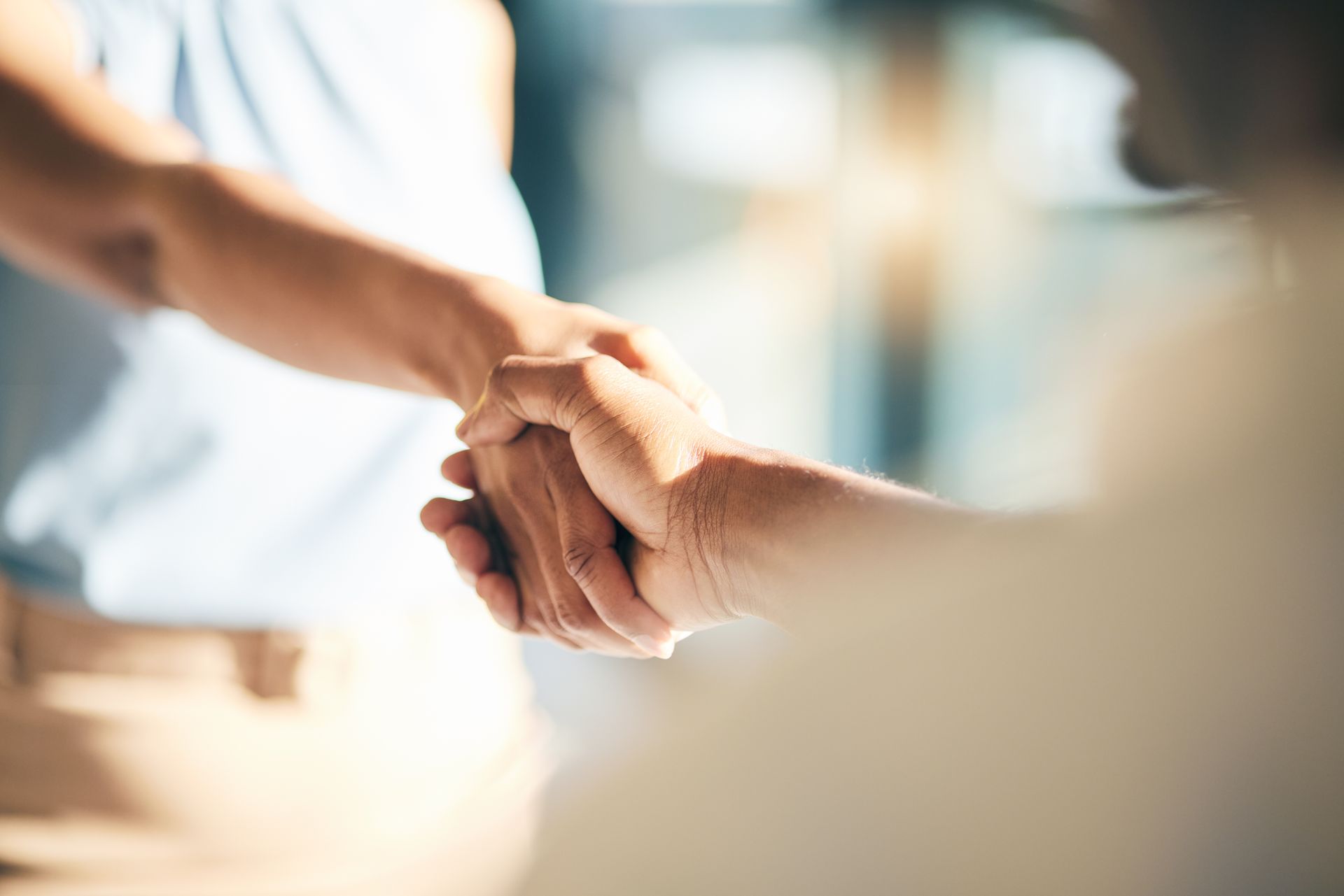 Two people shaking hands, blurred background suggests an office setting.