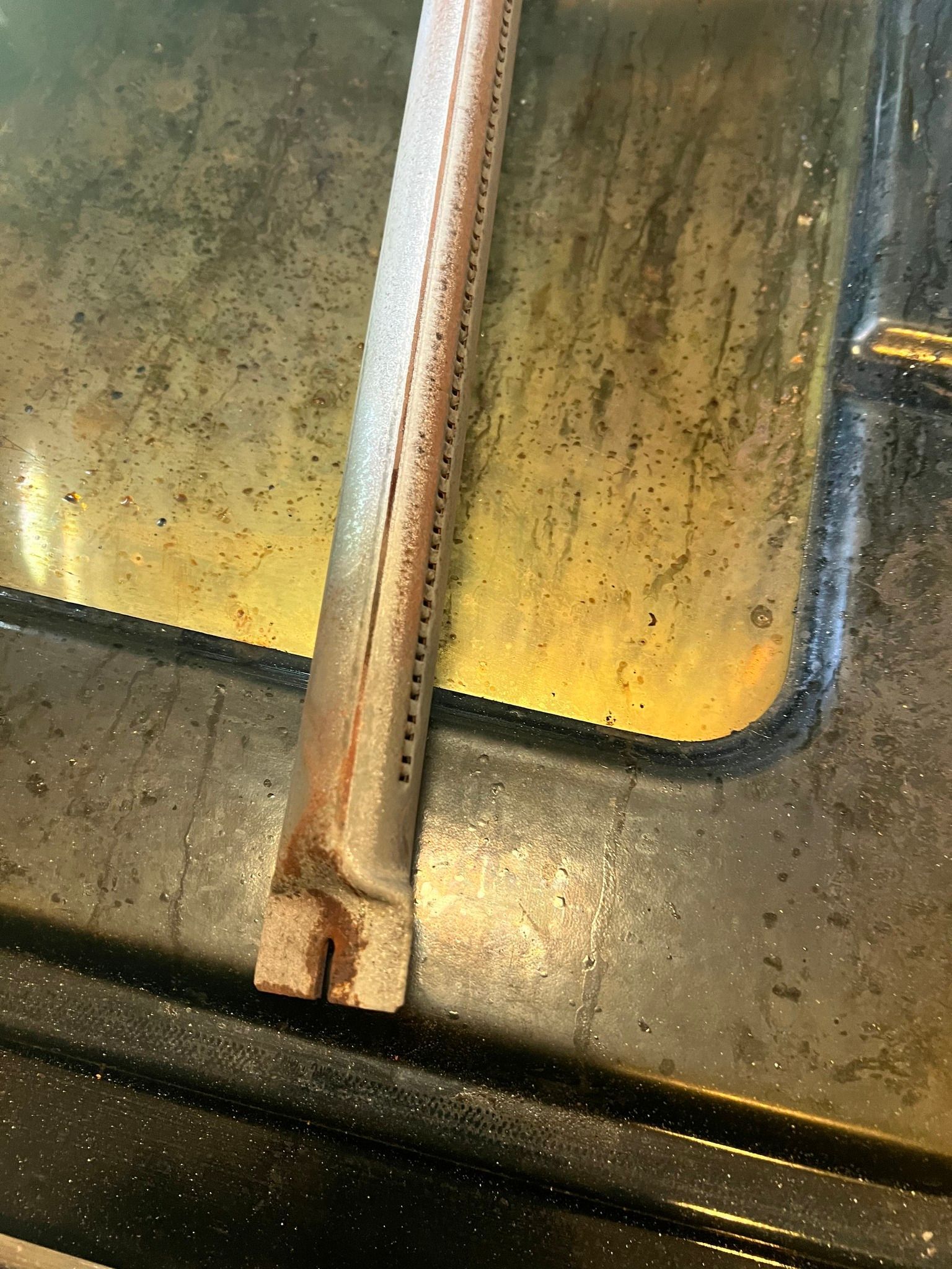 A close up of a dirty oven door with a burner sticking out of it.