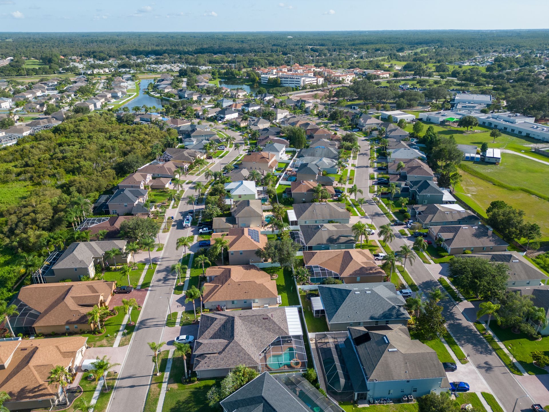 Aerial view of a residential neighborhood with houses, roads, and green spaces under a clear blue sky.