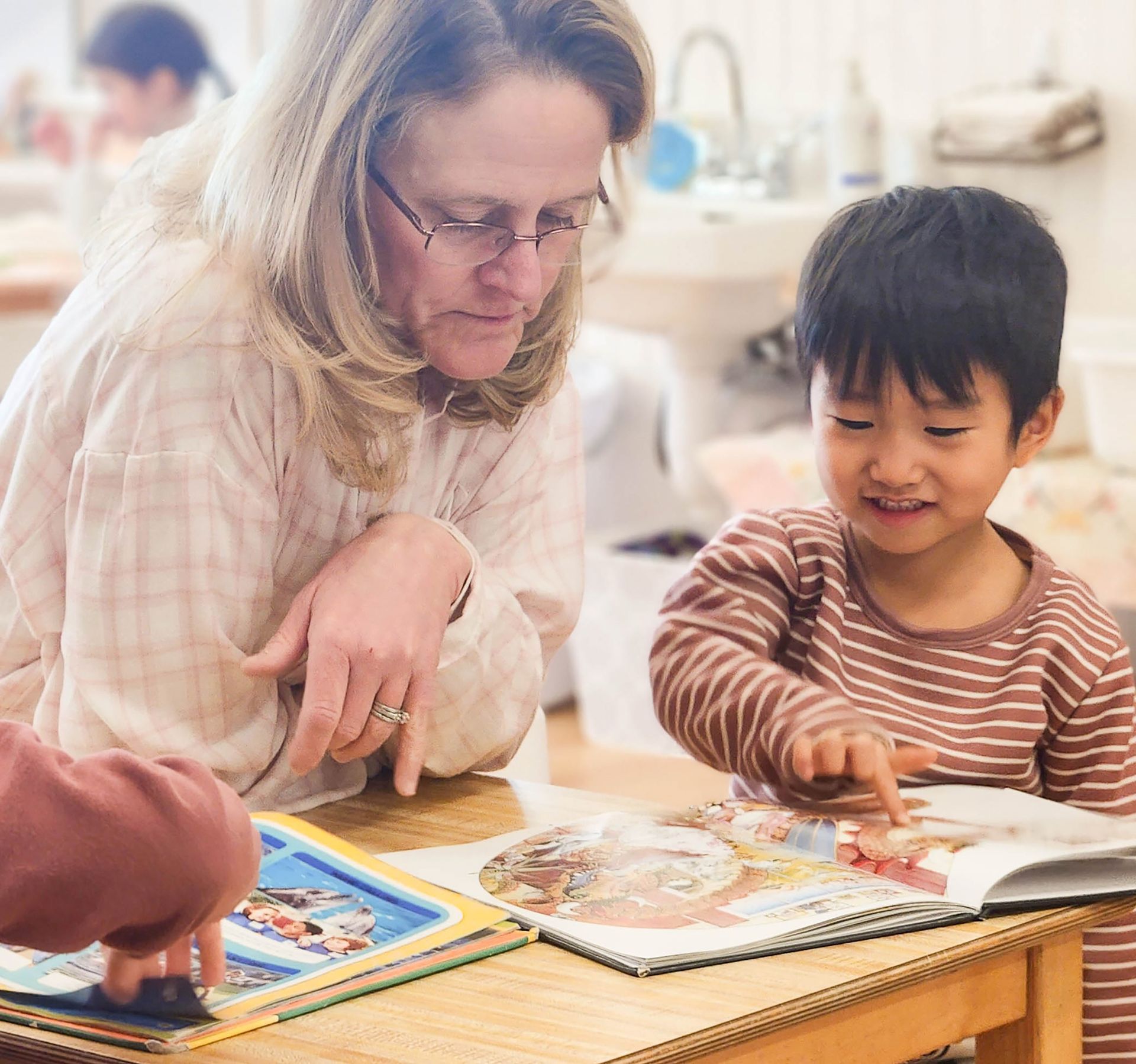Montessori guide and a child are sitting at a table looking at a book.