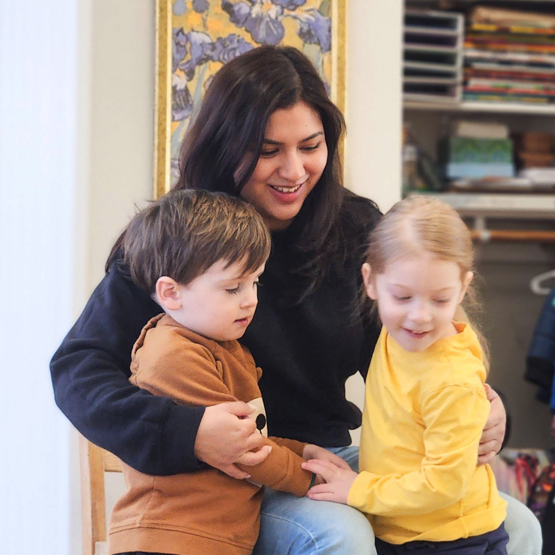 A Montessori guide is sitting on a chair with two Montessori children in the classroom.