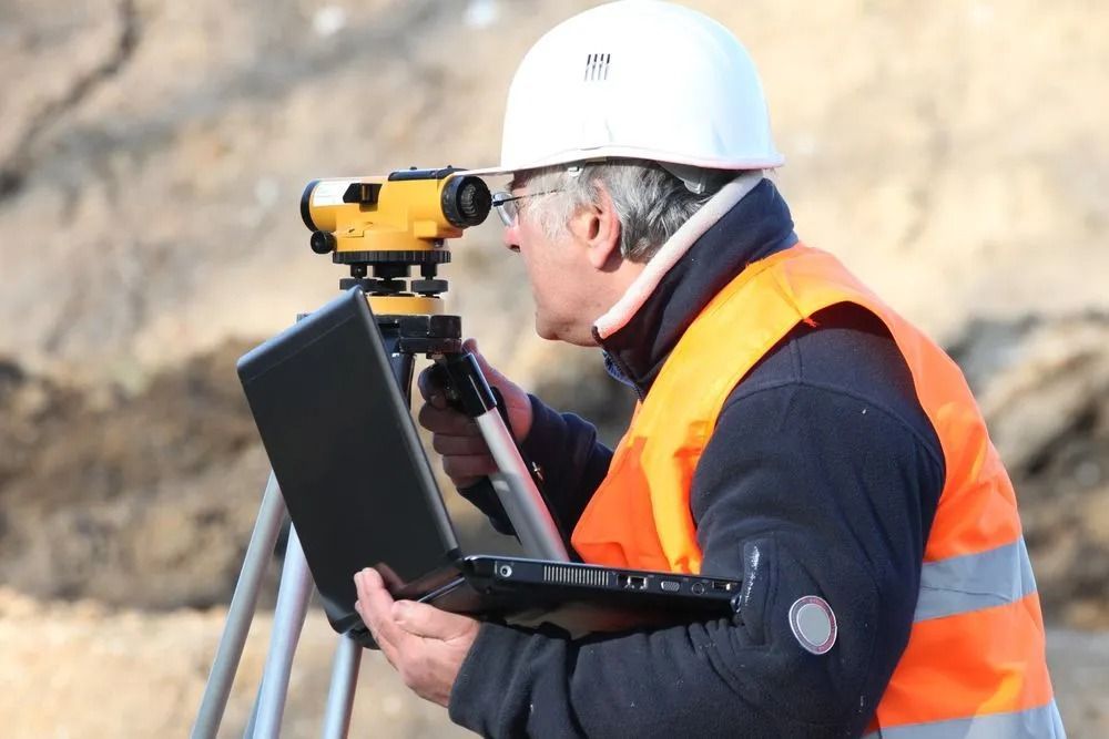 Surveyor in White Hard Hat and Orange Vest Using a Tripod-mounted — Coastal Surveying Group Pty Ltd In Brisbane, QLD