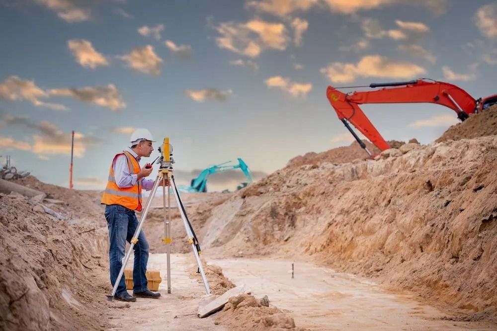 Surveyor Using Tripod at a Construction Site With an Orange Excavator — Coastal Surveying Group Pty Ltd In Baringa, QLD