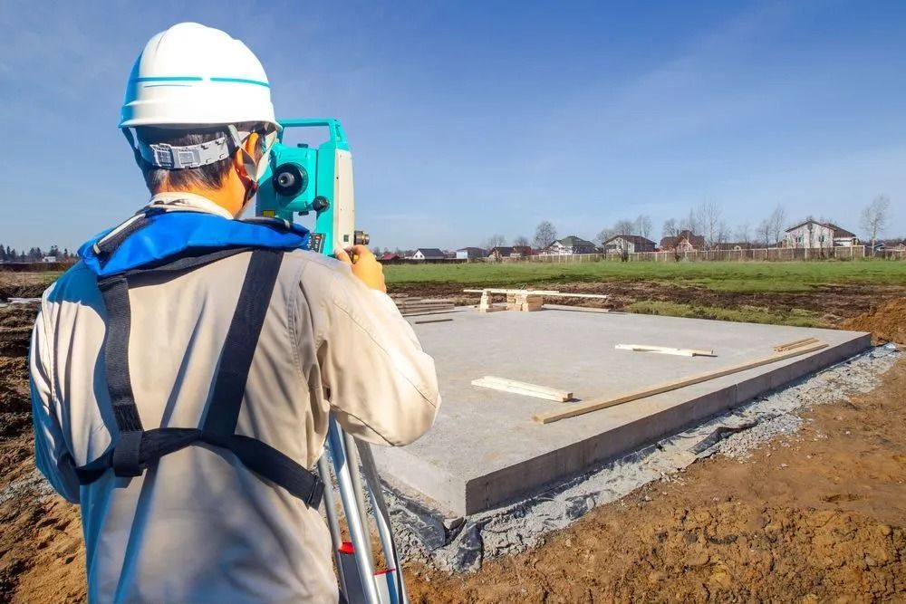 Surveyor in Hard Hat Using a Total Station Beside a Concrete Slab Foundation — Coastal Surveying Group Pty Ltd In Gympie, QLD