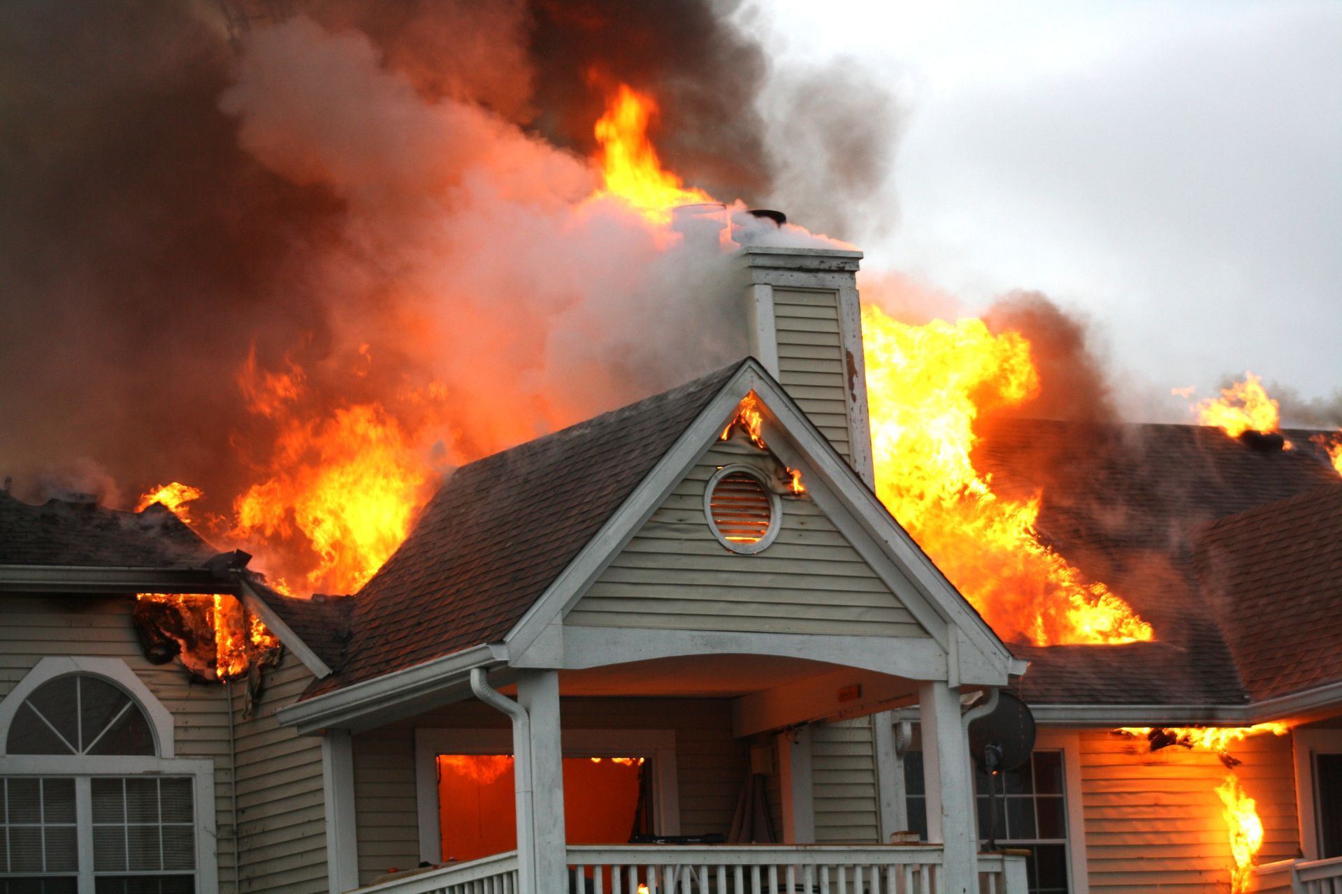 House engulfed in flames with thick smoke pouring from the roof and windows