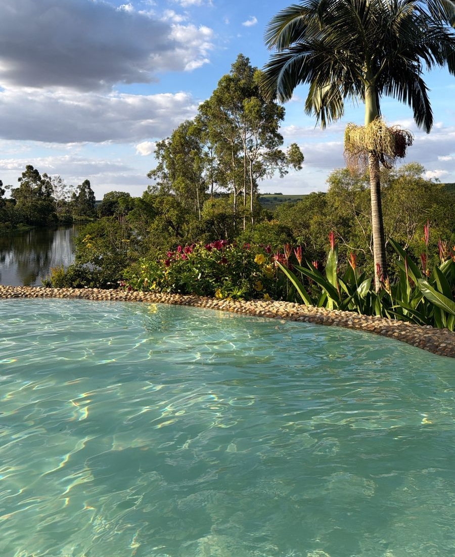 A piscina de água azul oferece vista para uma paisagem serena com um lago, árvores e céu nublado.