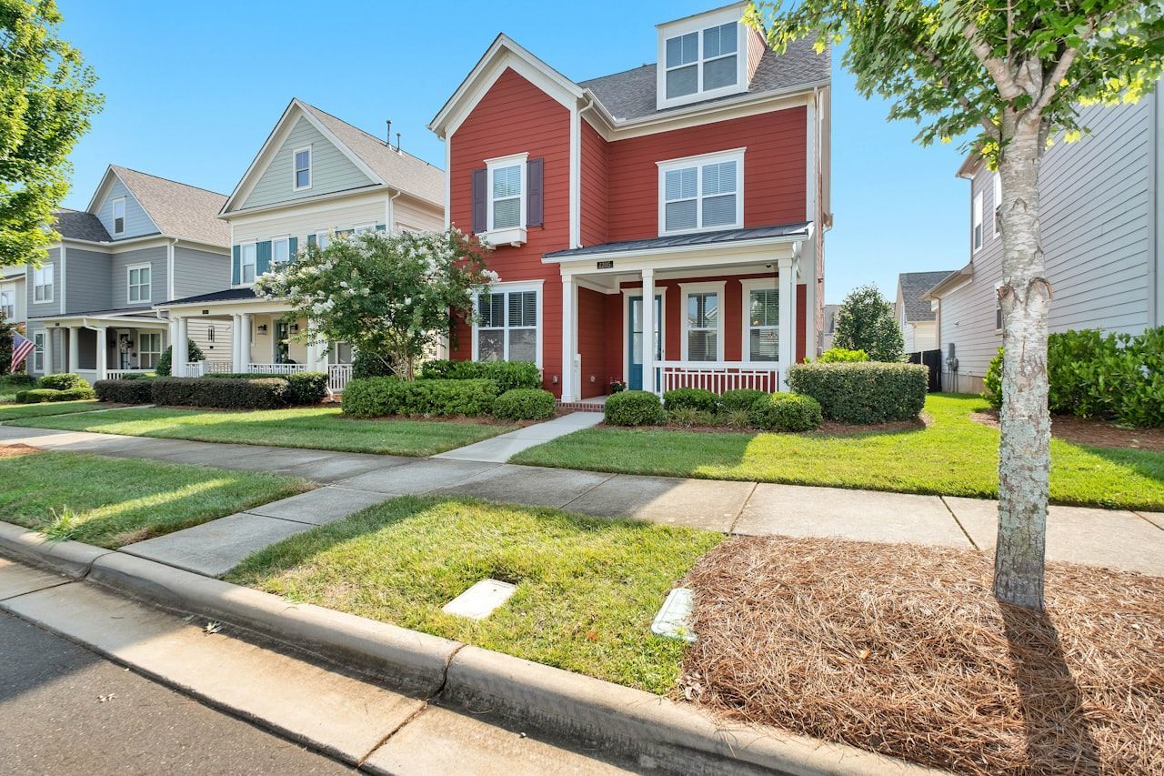 A red house with a white trim is sitting on a lush green lawn in a residential neighborhood.