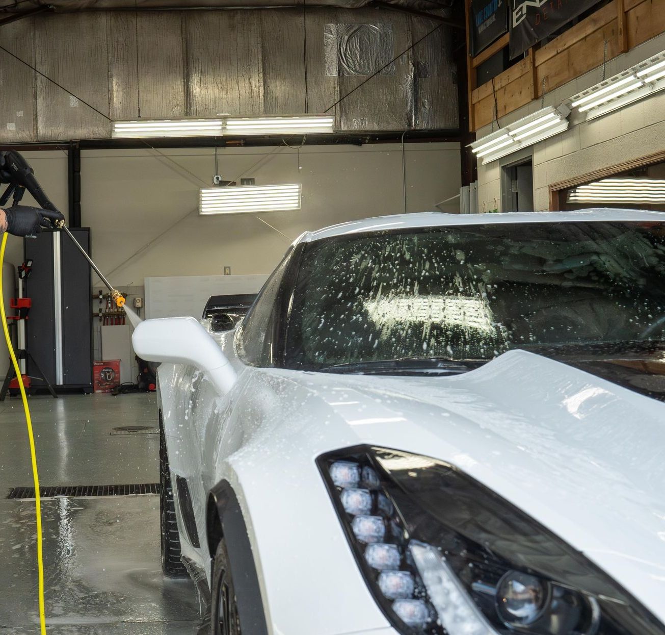 A man is washing a white sports car in a garage.