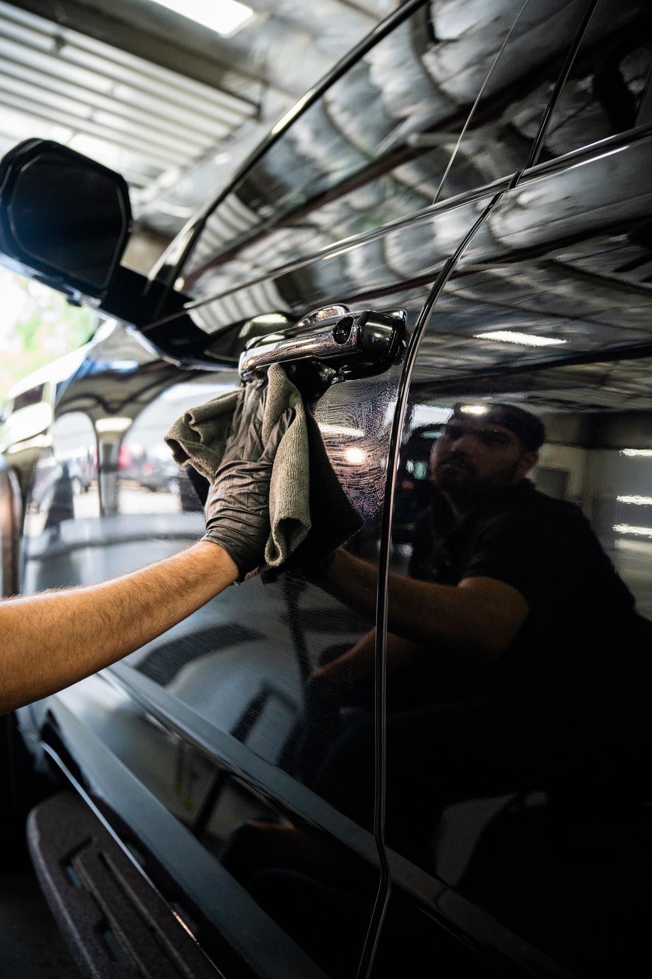 A man is cleaning a black car with a towel.