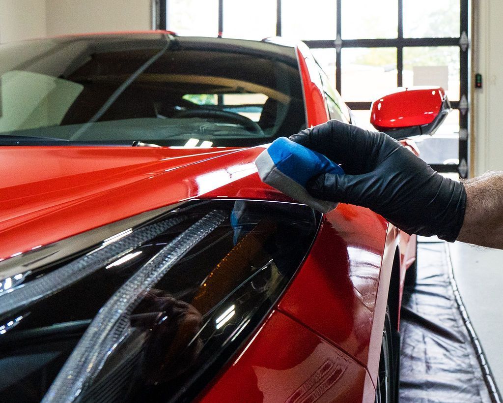 A person wearing black gloves is polishing a red car