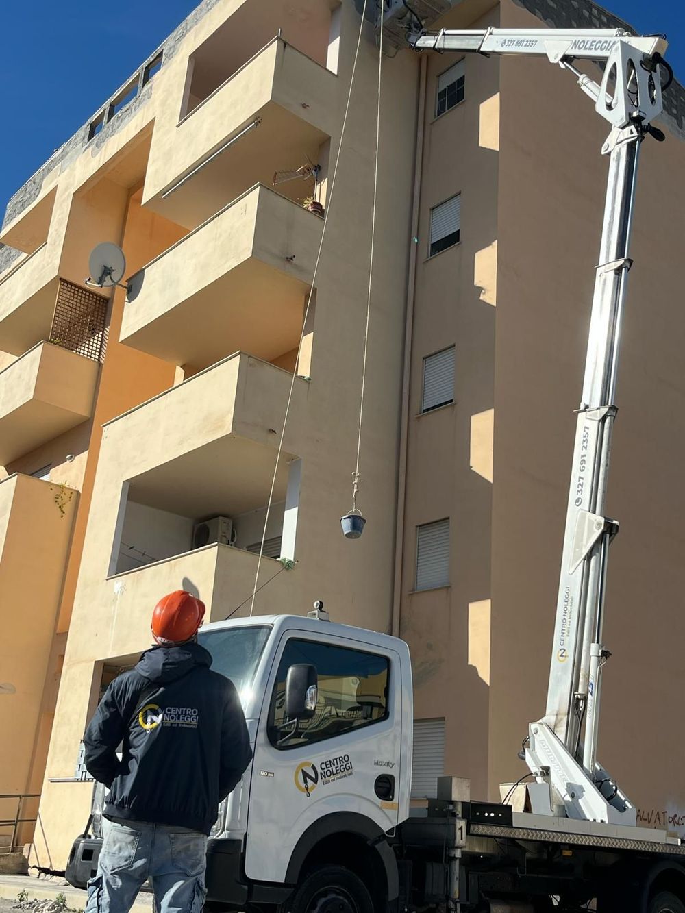 Un operaio aziona un sollevatore montato su un camion per spostare oggetti in un condominio beige.