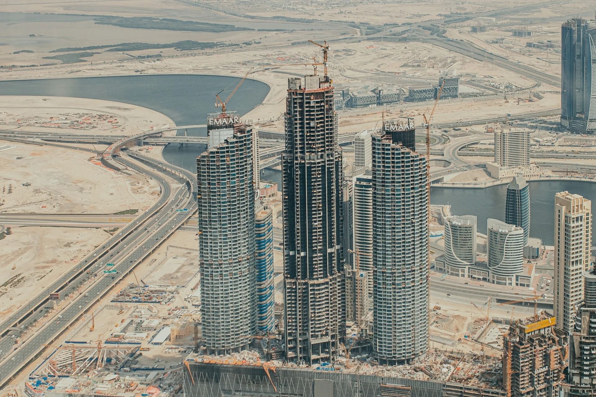 Aerial view of a high-rise building construction site in a desert city, with multiple towers and roads nearby