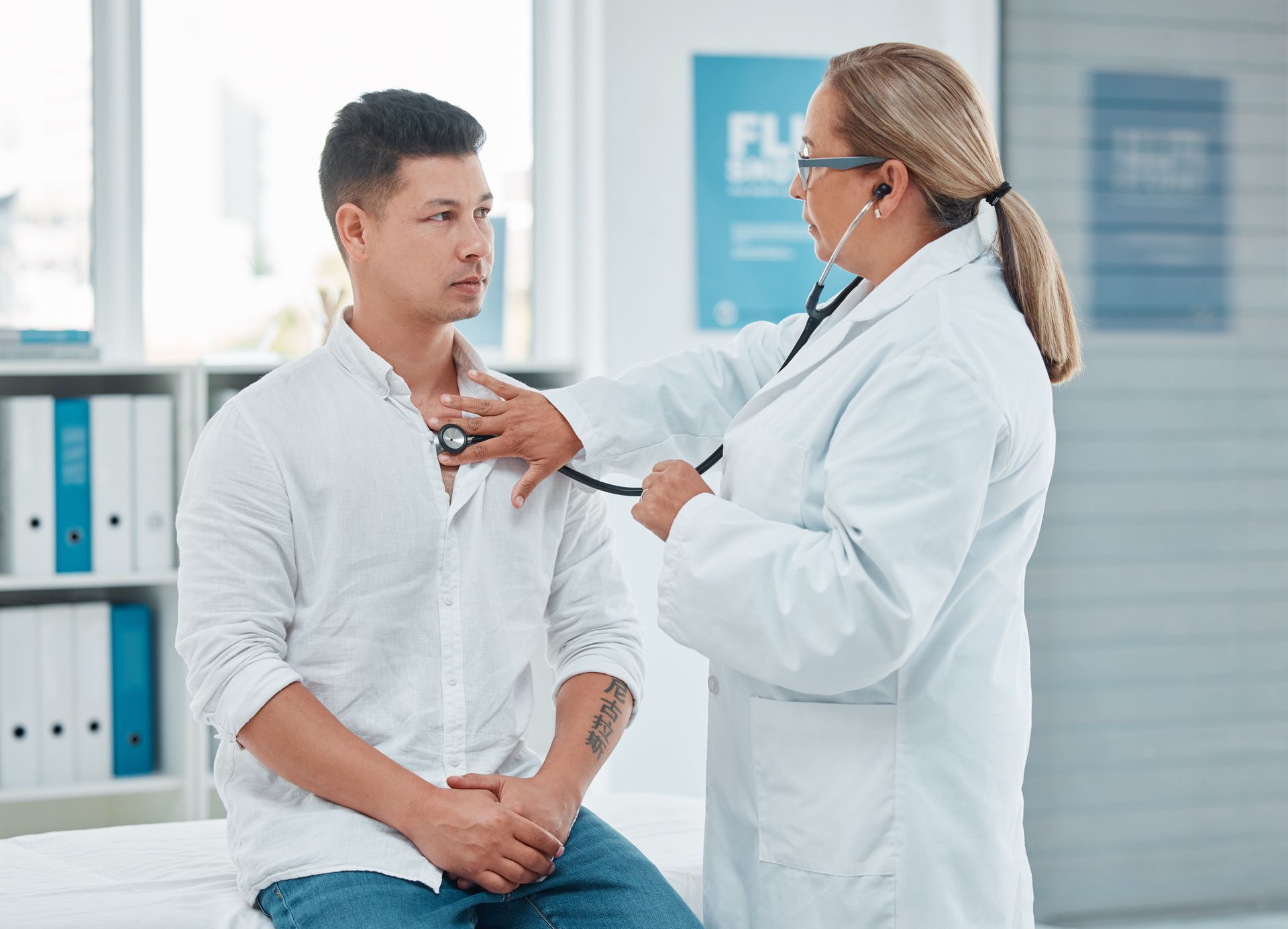 A doctor uses a stethoscope to examine a male patient undergoing an annual physical exam.