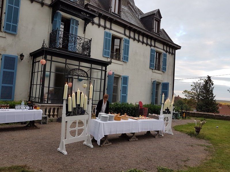 Een groot wit gebouw met blauwe luiken en een buffet ervoor.