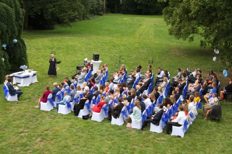 Een grote groep mensen zit op blauwe en witte stoelen in een veld