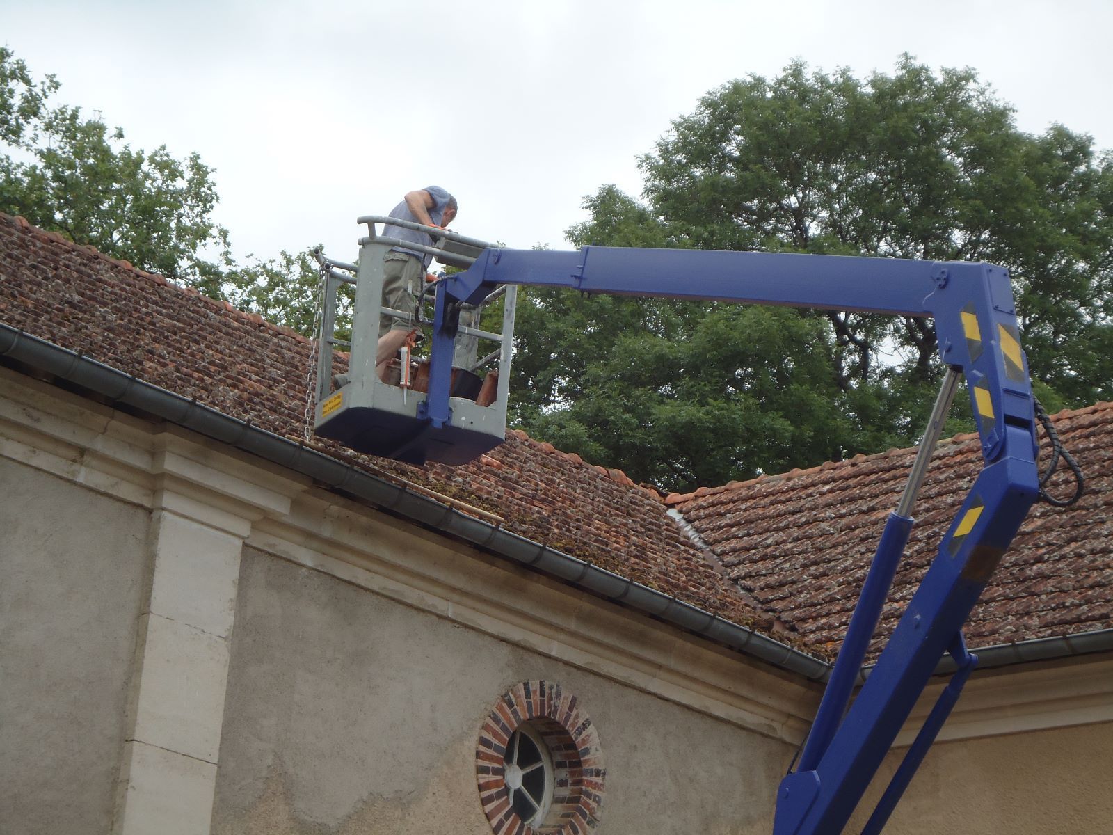 Een man werkt op een dak met een blauwe kraan