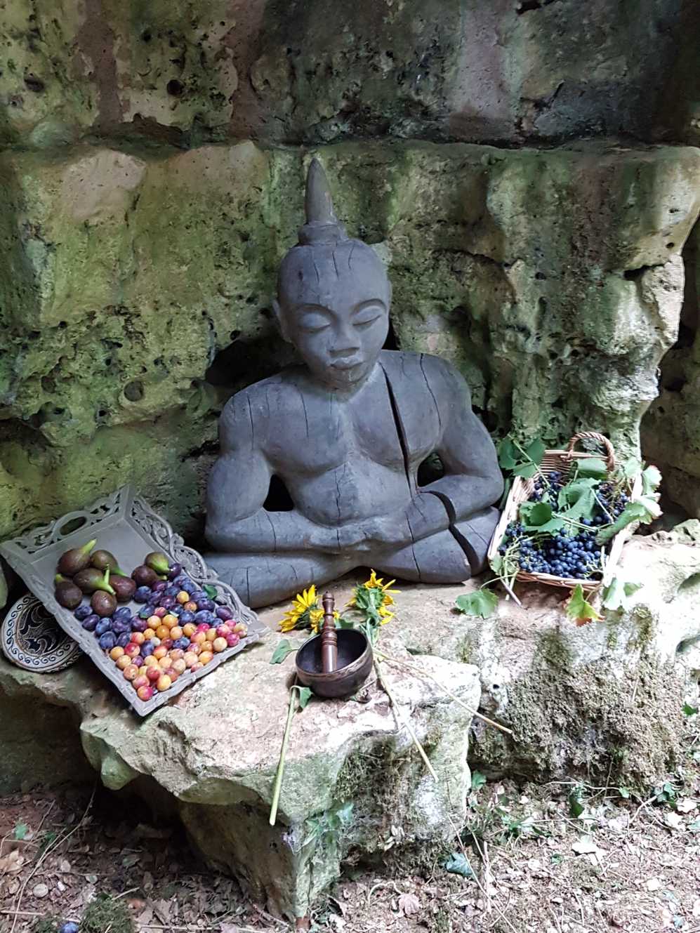 Een beeld van een man in lotushouding, omringd door fruit en bloemen.