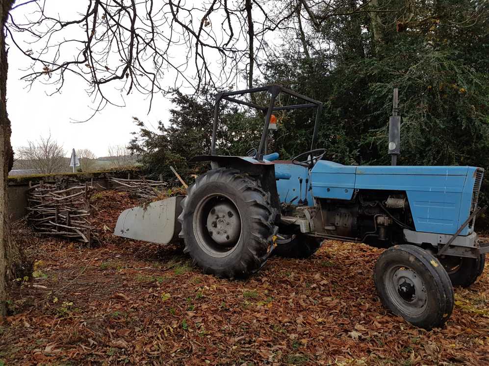 Een blauwe tractor staat geparkeerd in een stapel bladeren