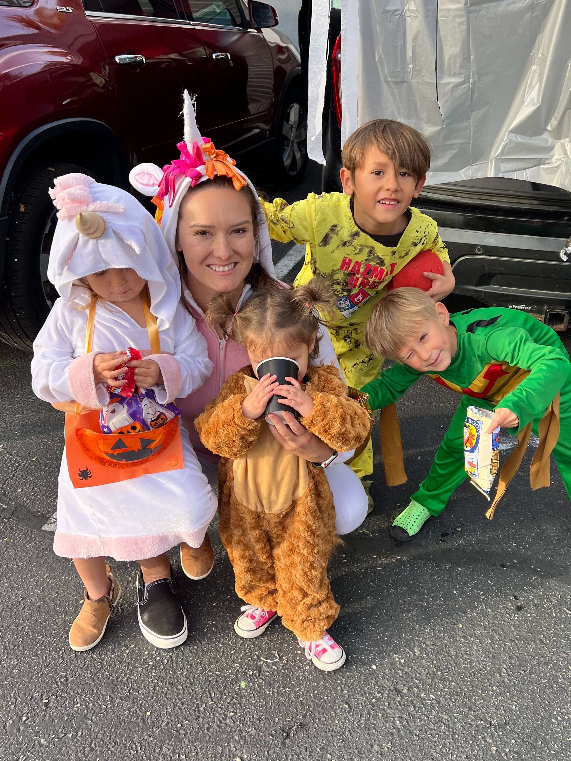 A woman is standing next to a group of children dressed in halloween costumes.