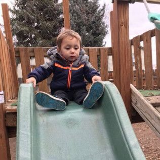 A Young Boy is Sitting on Top of a Slide at a Playground